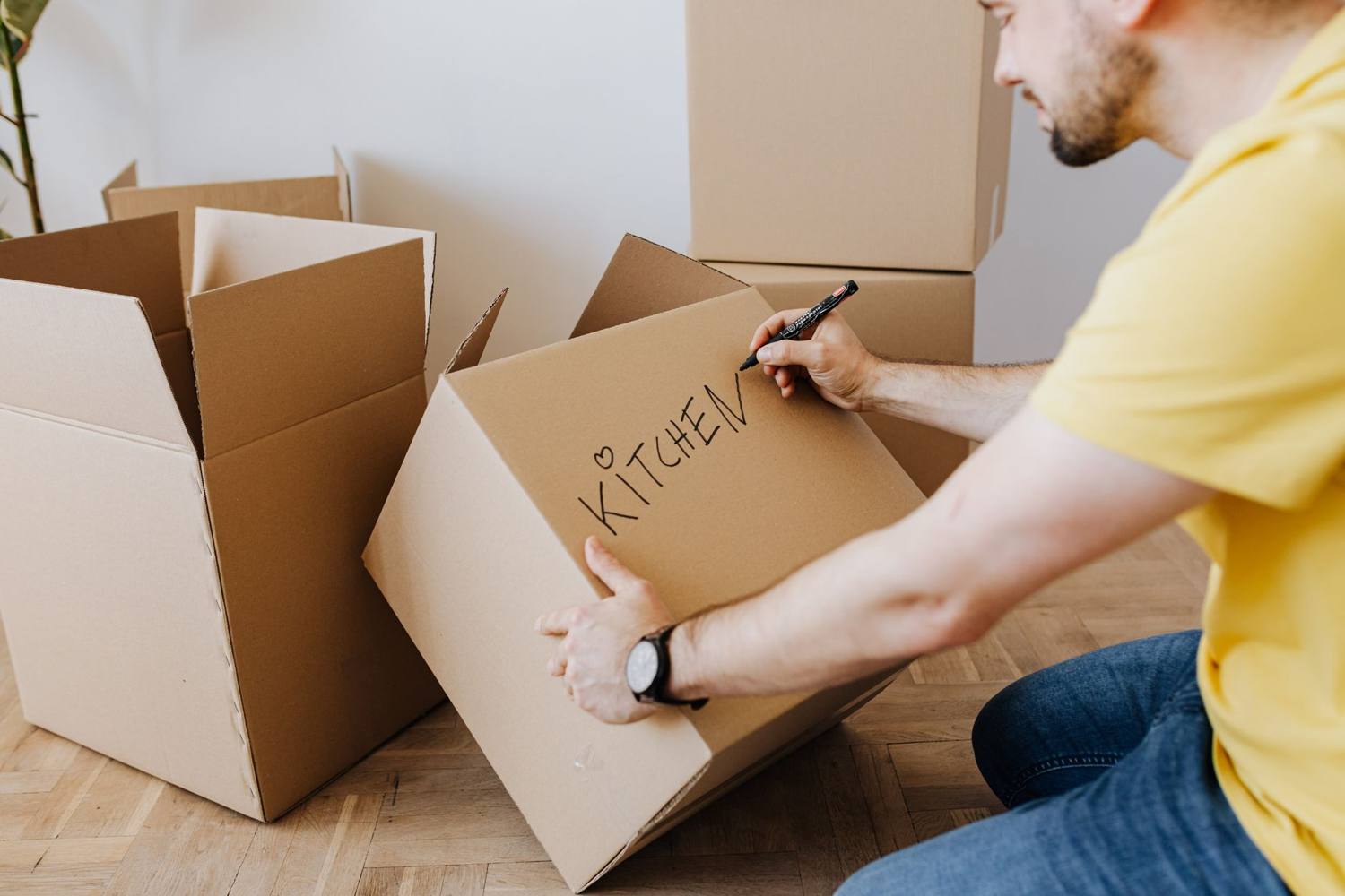 Homme adulte étiquetant des cartons pour les articles de cuisine lors d'un déménagement dans un nouveau foyer.